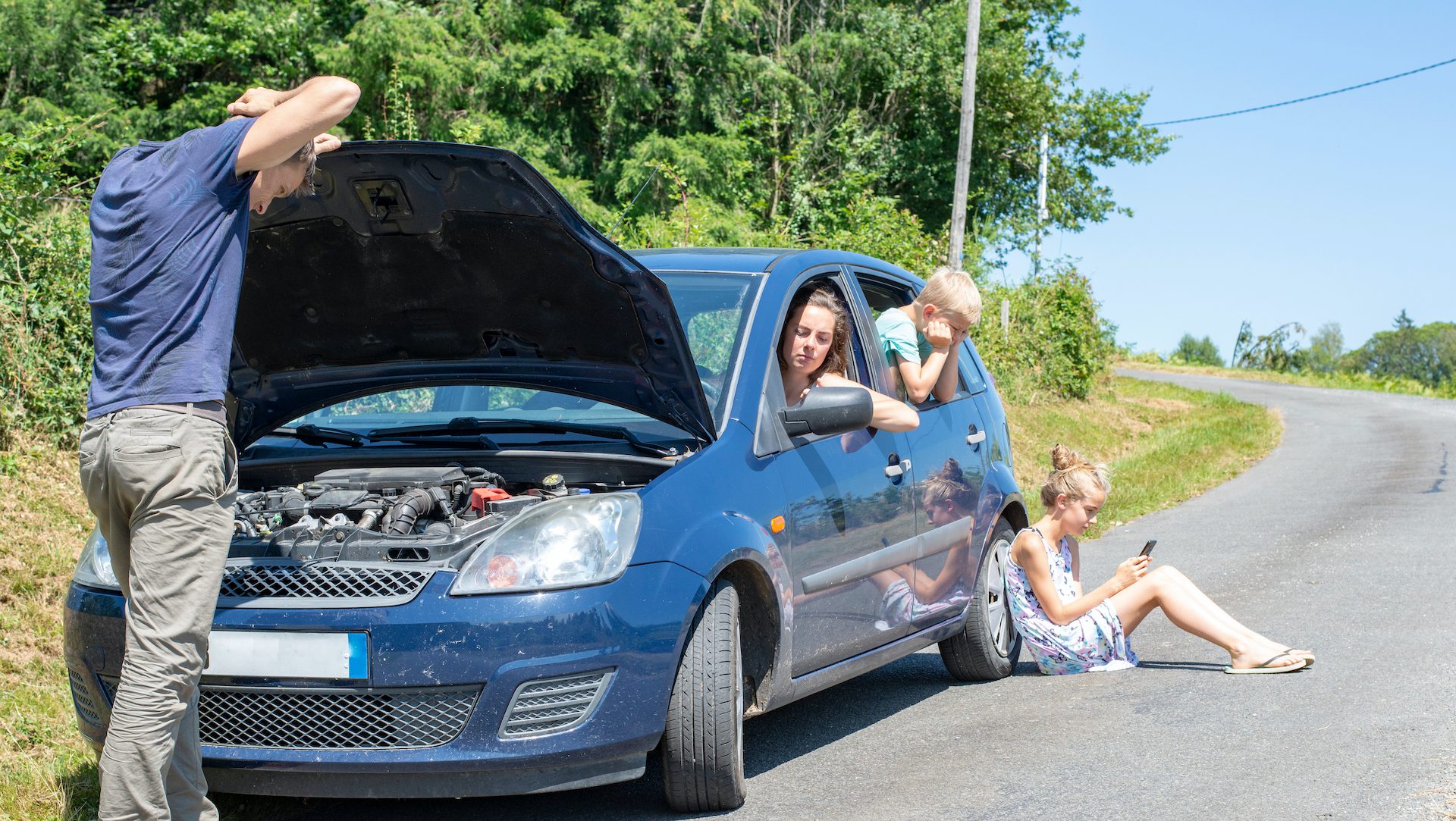 Family with broken down car on the side of the road on a summer family road trip