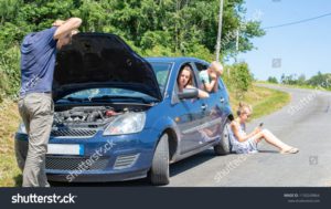 family sitting on side of road while car is broken down during family road trip