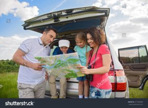 two parents and two children looking at a map while sitting in their car trunk during a family road trip