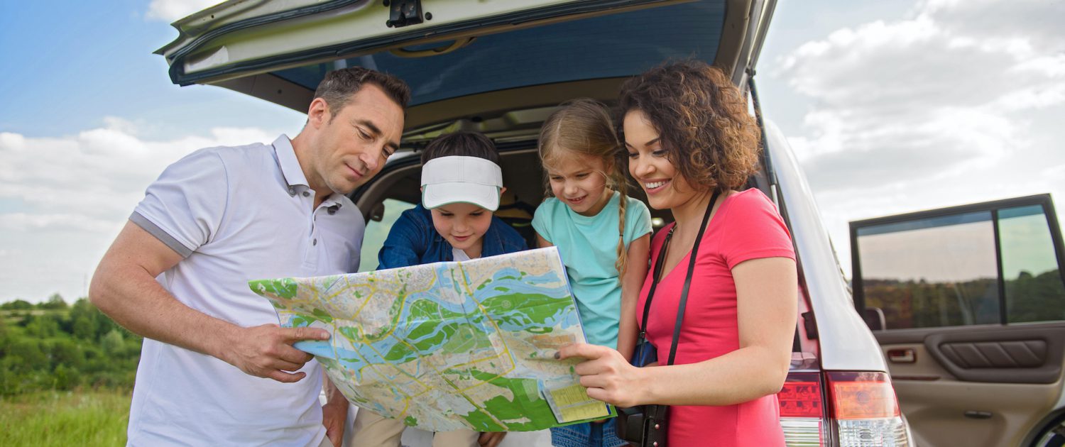 family of two children and two adults looking at a map on a family road trip