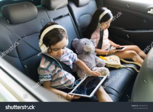 Two children in the back seat of a car entertaining themselves on a family road trip