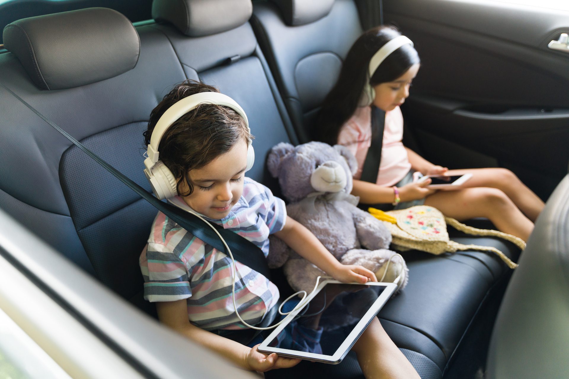 two children on their ipads being entertained in the back seat of a car on a family road trip