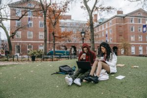 two college students sitting on the lawn on campus studying for class